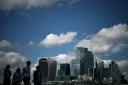 Des passants le long de la rive sud de la Tamise d'où l'on aperçoit le quartier des affaires et financier du centre de Londres, le 14 août 2025