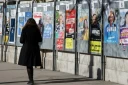 Une femme passe devant un panneau électoral avec les candidats à la mairie de Paris, le 9 mars 2026, à Paris