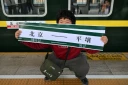 Un homme brandit une banderole "Pékin-Pyongyang" devant le train K27 à destination de Pyongyang, à la gare de Pékin, le 12 mars 2026 en Chine