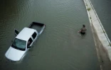 Un américain passe devant une voiture abandonnée alors que les eaux continuent de monter à Houston, le 28 août 2017