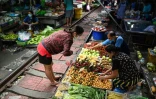 Une femme achète des légumes au marché de Maeklong, sur une voie de chemin de fer,  dans la province de Samut Songkhram, le 4 juin 2022 en Thaïlande