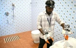 Un homme, caméra sur la tête et instruments dans les mains, se filme en train de plier des serviettes dans une salle d'eau reconstituée dans le labo de la société Objectways, à Karur, en Inde, le 13 mai 2026