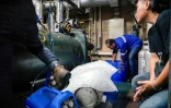 Des techniciens de la société Recoolit travaillent à capturer les gaz de refroidissemen d'une grande unité de climatisation au sous-sol d'un complexe d'habitation à Jakarta, le 10 juin 2025 en Indonésie