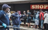 Un policier pointe son arme sur des clients d'un supermarché pour leur faire respecter la distanciation sociale, à Johannesburg, le 28 mars 2020