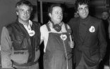 Michel Sardou entre Coluche et Enrico Macias (D) à Paris, le 14 décembre 1985, sur le plateau d'Europe 1, où ils sont venus soutenir la campagne en faveur des restos du coeur