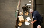 Un  agent de la douane américaine, aidé par un berger allemand, cherche de la drogue dans des paquets arrivés au centre de tri postal de l'aéroport John F. Kennedy, le 24 juin 2019 à New York
