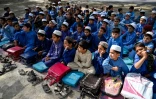 Des écoliers portent des tuniques et chapeaux selon le nouveau code d'uniforme, lors d'une classe en extérieur, dans le district de Mohmand Dara, le 20 avril 2025 en Afghanistan