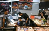 Napat Mitmakorn (c),9 ans, travaille sur le tatouage de son oncle avec son père Nattawut Sangtong (d) lors de la 2025 Thailand Tattoo Expo à Bangkok, le 15 mars 2025 en Thaïlande