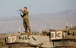 Un soldat israélien dispose un drapeau sur un char durant un exercice militaire en Galilée, près de la frontière avec le Liban, le 26 octobre 2023