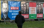 Un piéton devant des panneaux d'affichage gouvernementaux montrant le président ukrainien Volodymyr Zelensky (à gauche), avec le texte "Ne laissons pas Zelensky avoir le dernier mot", et une autre affiche montrant la présidente de la Commission européenne Ursula von der Leyen (à droite), le président ukrainien Volodymyr Zelensky (au centre) et le chef de l'opposition hongroise Peter Magyar (à gauche) avec le texte "Ils sont eux-mêmes le risque", à Budapest le 3 mars 2026