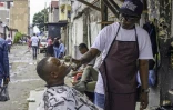 Un coiffeur de rue pulvérise de l'alcool sur le visage d'un client sur un trottoir à Kinshasa, le 17 octobre 2024 en RDC