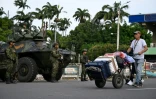 Un homme chargé de valises sur un diable passe devant des militaires colombiens stationnés à Cucuta, à la frontière avec le Venezuela, le 3 janvier 2026 
