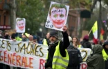 A Toulouse, un "gilet jaune" brandit un portrait d'Emmanuel Macron maquillé en "joker", le 16 novembre 2019, pour le premieer anniversaire du mouvement de contestation sociale