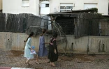 Des habitants de la ville de Sdérot dans le sud d'Israël passent devant une clôture endommagée par la chute d'une roquette tirée de la bande de Gaza, le 14 juillet 2018