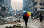 Un homme marche avec un parapluie aux couleurs de l'arc-en-ciel sur une rue boueuse au milieu des décombres dans le nord de Gaza, le 10 février 2025