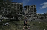 Une femme marche à Bilozerske, près de bâtiment bombardés par la Russie, le 12 août 2025