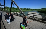 Des personnes traversent le pont en bois sur la rivière Tisa au poste frontière de Sighetu Marmatiei entre la Roumanie et l’Ukraine, le 17 mai 2024