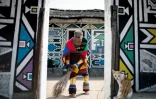 Dans sa jupe traditionnelle à perles, le cou et les jambes encerclés d'anneaux de cuivre, Esther Mahlangu balaie la cour devant sa hutte.