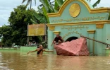 Un moine bouddhiste patauge dans les eaux tandis qu'un autre est assis sur un toit brisé devant un monastère dans le village de Sin Thay à Pyinmana, dans la région de Naypyidaw en Birmanie, le 13 septembre 2024