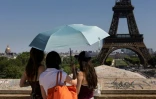 Des touristes se protègent du soleil sous un paraplluie devant la Tour Eiffel lors d'une vague de chaleur à Paris, le 27 mai 2026