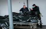 Un policier prend une photo d'une personne décédée placée dans une housse mortuaire, devant la morgue de Boutcha, en Ukraine, le 18 avril 2022