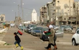 Des Libyens brandissent des drapeaux en passant devant des bâtiments endommagés pour participer aux célébrations le 17 février 2022 à Benghazi, dans l'est de la Libye du 11e anniversaire de la révolte contre le colonel Mouammar Kadhafi