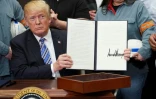 Le président américain Donald Trump montre le document qu'il vient de signer instaurant des taxes sur les importations d'acier et d'aluminium, le 8 mars 2018 à la Maison Blanche, à Washington