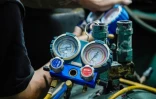Des techniciens de la société Recoolit suivent sur des jauges le captage des gaz de refroidissemen d'une grande unité de climatisation au sous-sol d'un complexe d'habitation à Jakarta, le 10 juin 2025 en Indonésie