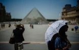 Une touriste se protège du soleil sous une ombrelle devant la Pyramide du Louvre, à Paris, le 23 juin 2026