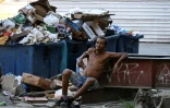 Un sans-abri assis devant des conteneurs à ordures dans une rue de La Havane, le 21 juillet 2025 à Cuba