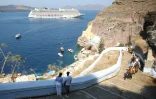 Des touristes grimpent vers le village de Fira, alors qu'un bateau de croisière arrive, sur l'île grecque de Santorin, le 20 juillet 2024