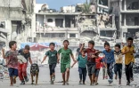 Des enfants courent avec un chien au milieu de bâtiments détruits dans une rue de Khan Younès, dans le sud de la bande de Gaza, le 8 juillet 2024
