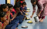 Des élèves en prières avant un petit déjeuner à "l'école du feu rouge", qui accueille des enfants défavorisés dans des conteneurs aménagés en salles de cours sous un pont autoroutier, le 18 mai 2026 à Bombay