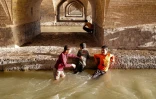 Des enfants jouent sous les arches du pont historique Si-o-Se Pol, dans les eaux de la rivière Zayandeh-roud, à Ispahan dans le centre de l'Iran, le 15 mai 2022
