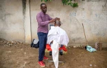 Papy Kalume, un coiffeur de rue, coupe les cheveux d'un client sur le trottoir Ă Kinshasa, le 17 octobre 2024 en RDC