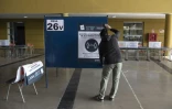 Pose d'une affiche sur un isoloir, dans un bureau de vote à Santiago du Chili, le 14 mai 2021