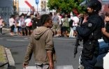 Un policier parle avec un habitant à Noumea en Nouvelle-Calédonie devant une file d'attente pour entrer dans un supermarché le 18 mai 2024