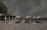 La fumée d'un feu de forêt s'élève derrière un bar de plage du village de Vatera, dans l'est de la station balnéaire populaire de l'île grecque de Lesbos, le 23 juillet 2022
