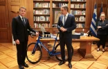 Le président français Emmanuel Macron (G) offre un vélo produit en France au Premier ministre grec Kyriakos Mitsotakis à l'issue d'un déjeuner de travail, le 25 avril 2026 à Athènes 