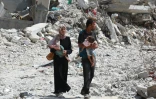 Un couple palestinien tenant ses enfants dans les bras marche au milieu des destructions à Khan Younès, dans le sud de la bande de Gaza, le 4 juillet 2024