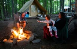 Une famille autour d'un feu de camp devant leur tente du camping Huttopia, le 14 août 2019 à Sutton, au Canada,