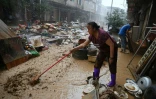 Une habitante repousse la boue dans une zone inondée après la rupture d'un réservoir près de Gantang, dans la région du Guangxi, le 9 juillet 2026 dans le sud-ouest de la Chine