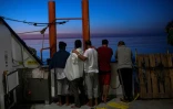 Des migrants regardent le soleil levant à bord de l'Aquarius en mer Méditerrannée le 16 août 2017