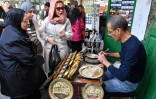 Des femmes observent un artisan qui grave un dessin sur un plat en cuivre dans sa boutique des souks de la médina de Tunis, le 7 décembre 2023
