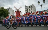 Le Français Valentin Madouas passe devant les danseuses du cabaret du Moulin Rouge à Montmartre lors de la course en ligne hommes des Jeux olympiques de Paris le 3 août 2024
