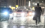 Des voitures dépassent un piéton sur une route inondée près de la station de métro de Chiba, dans la ville de Chiba à l'est de Tokyo, le 13 août 2026, alors que de fortes pluies s'abattent sur la région