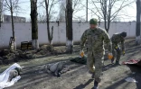 Des soldats ukrainiens passent devant les dépouilles de soldats ukrainiens près d'une caserne militaire touchée par des roquettes russes, à Mykolaïv, dans le sud de l'Ukraine, le 19 mars 2022