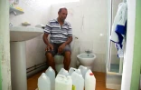 Un habitant pose avec ses bidons utilisés pour stocker l'eau dans sa salle de bain à Capesterre, en Guadeloupe, le 26 juillet 2018
