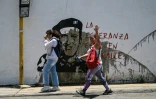 Deux femmes passent devant un graffitti représentant l'ancien président vénézuélien Hugo Chavez, accompagné de la phrase: "L'espoir est dans la rue", dans le bidonville de Petare, dans l'est de Caracas, le 1er août 2024.