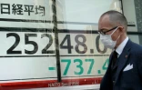Un passant marche devant un écran affichant les cours des indices boursiers, le 7 mars 2022 à Tokyo